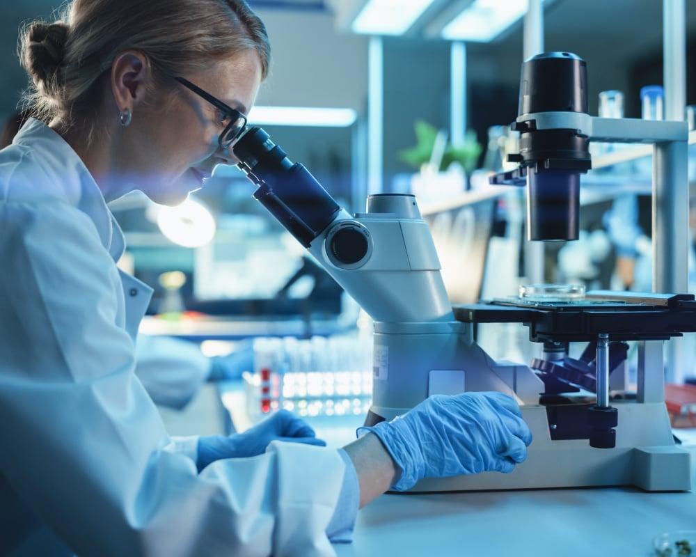 Scientist wearing glasses and latex gloves looking through a microscope