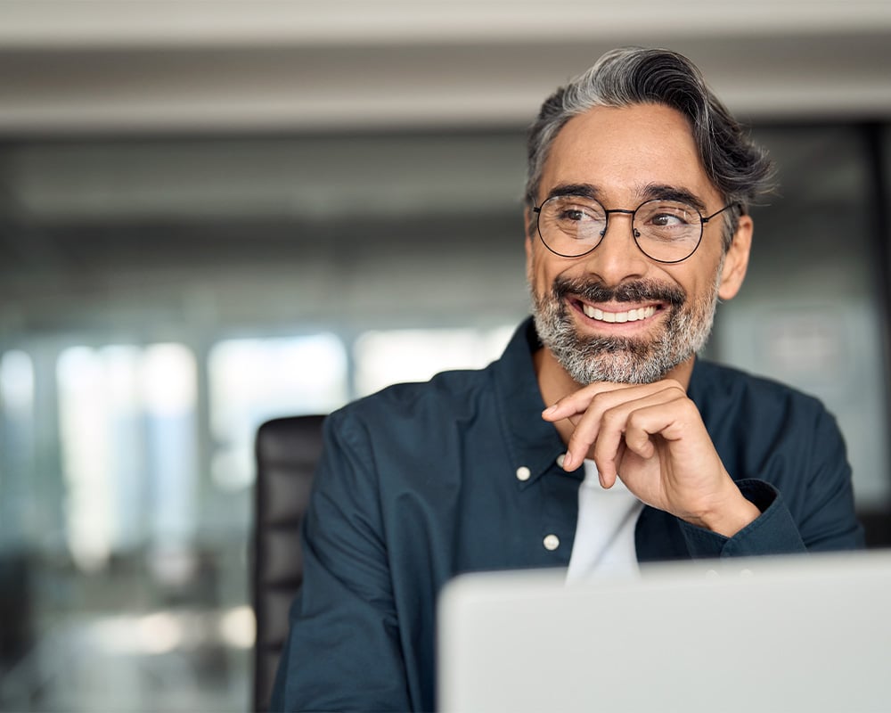 Man with glasses smiling looking over his computer.